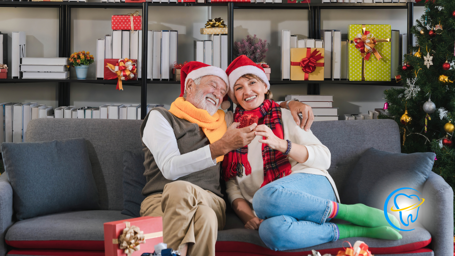 An elderly couple is sitting on a couch in front of a christmas tree.