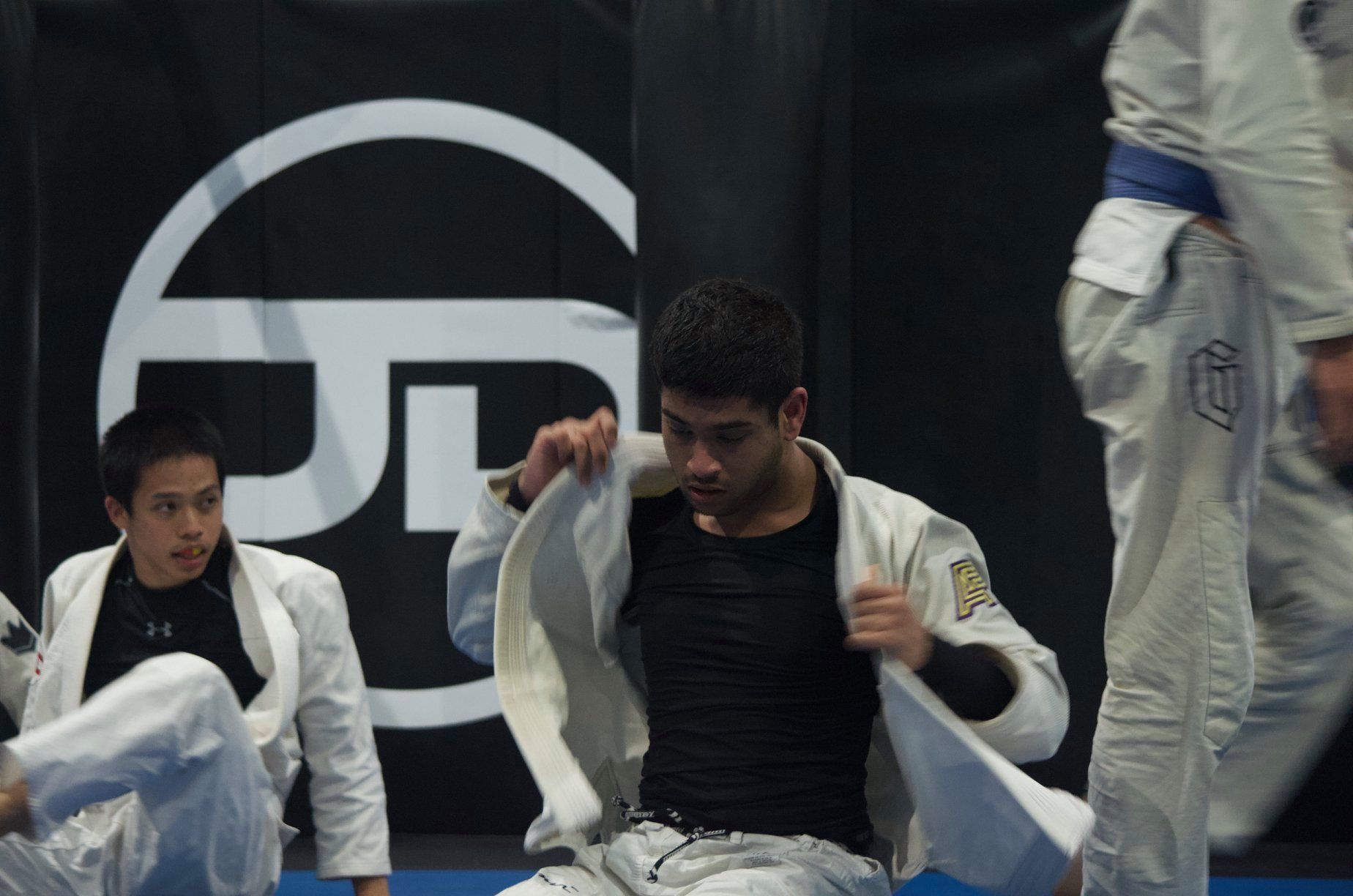 A group of men are practicing jiu jitsu in front of a sign that has the letter g on it
