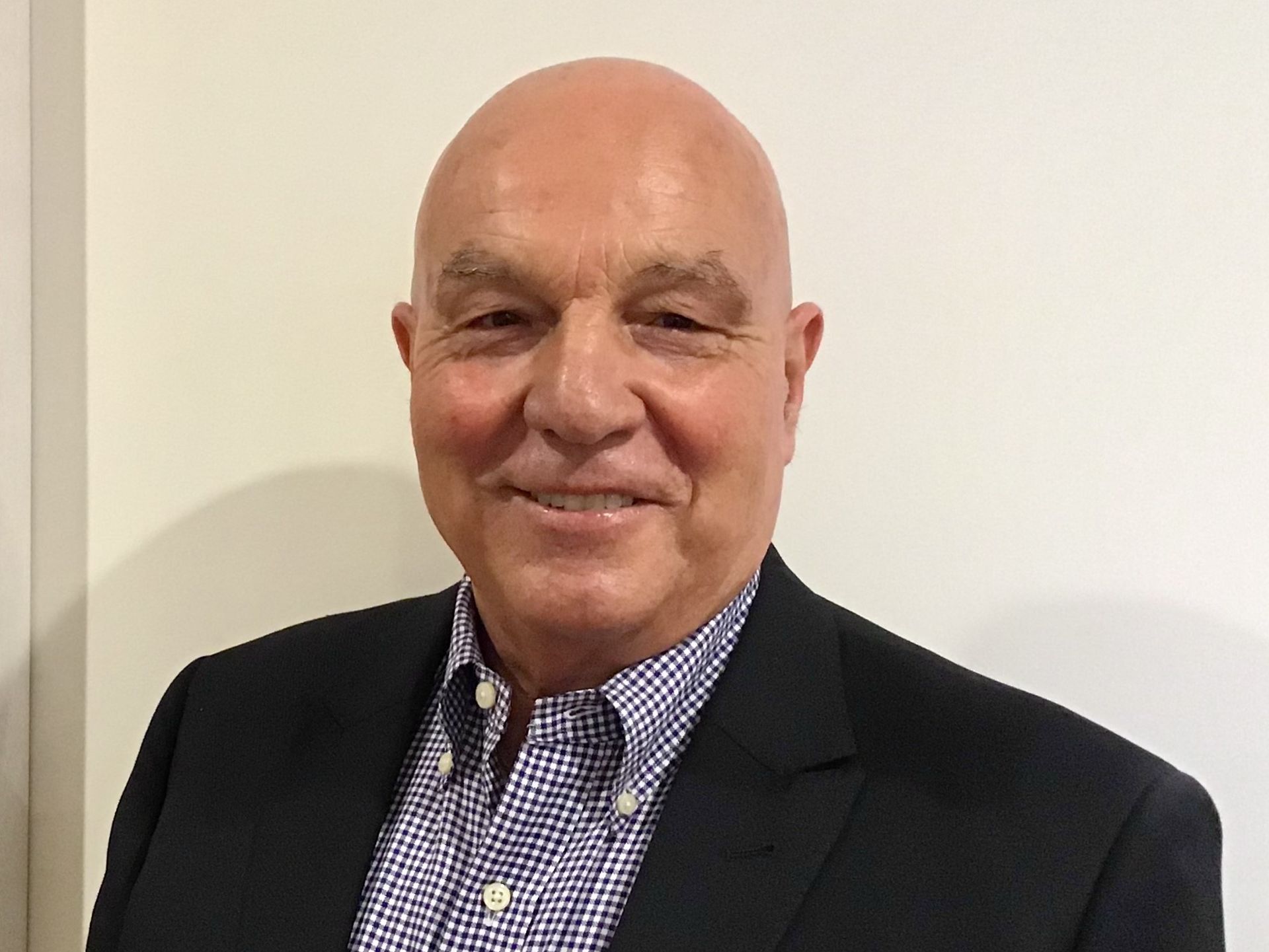 A bald man in a suit and plaid shirt is smiling for the camera.