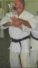 A man with a beard is wearing a white karate uniform and a black belt.