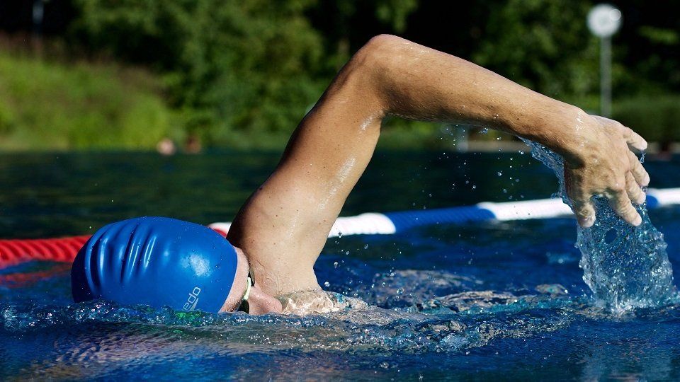 A person wearing a blue swim cap is swimming in a pool