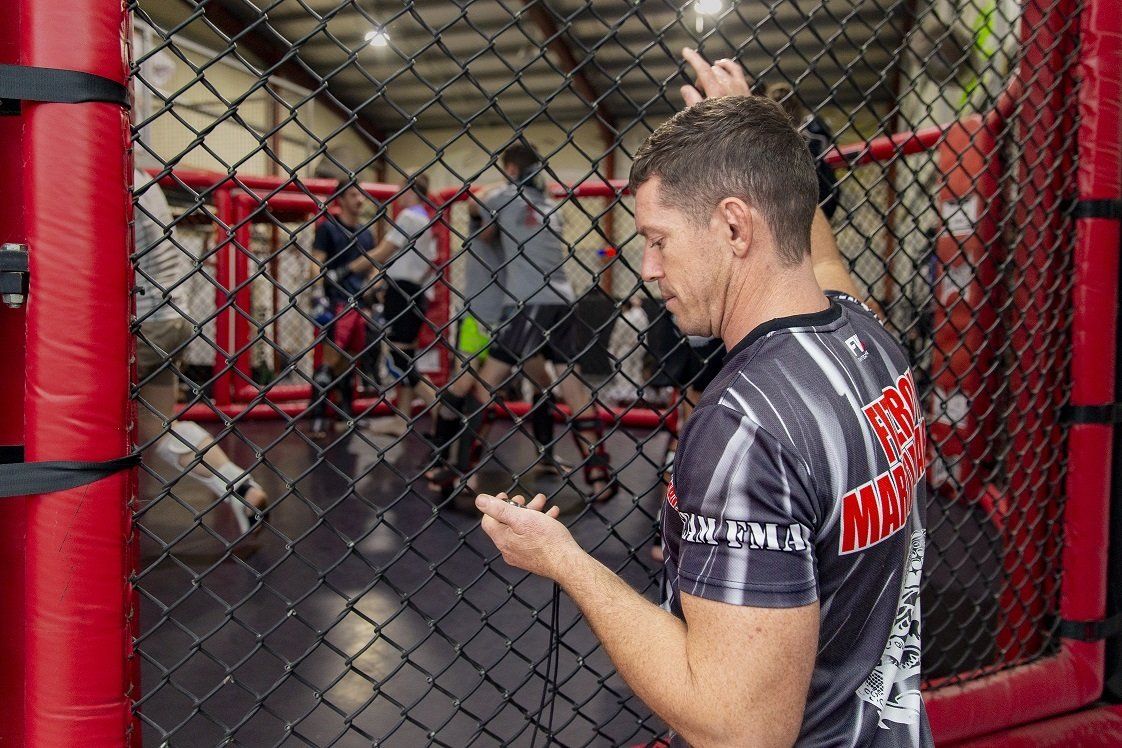 A man is standing in a boxing ring looking at his phone.