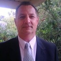 A man in a suit and tie is standing in front of trees.