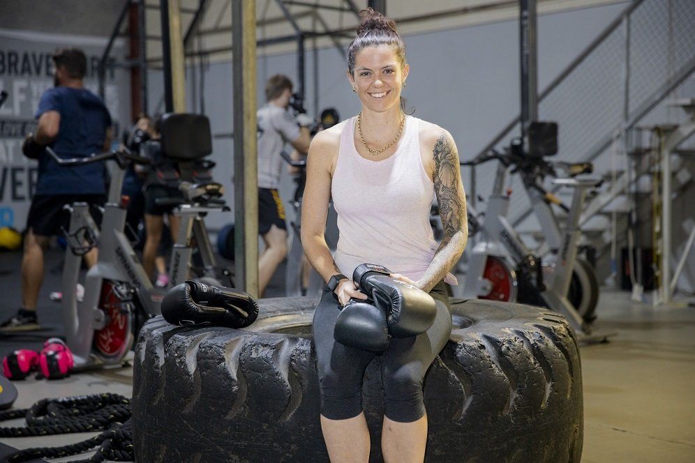 A woman is sitting on a tire in a gym holding boxing gloves.