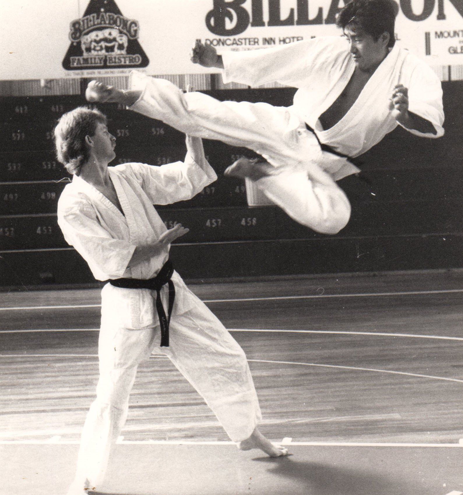 Two men are practicing martial arts in front of a sign that says billabong
