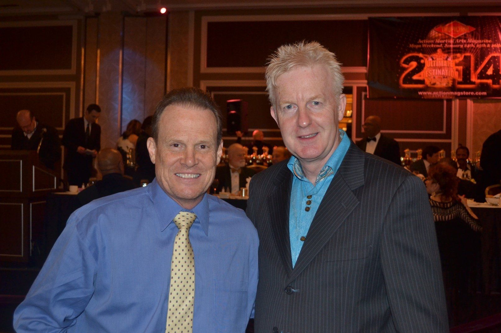 Two men are posing for a picture in front of a sign that says 2014