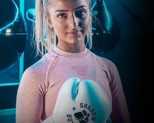 A woman in a pink shirt is holding a pair of boxing gloves.