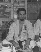 A man in a karate uniform is sitting on the floor in a black and white photo.