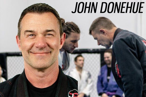 A man is smiling in front of a group of men in a boxing ring.