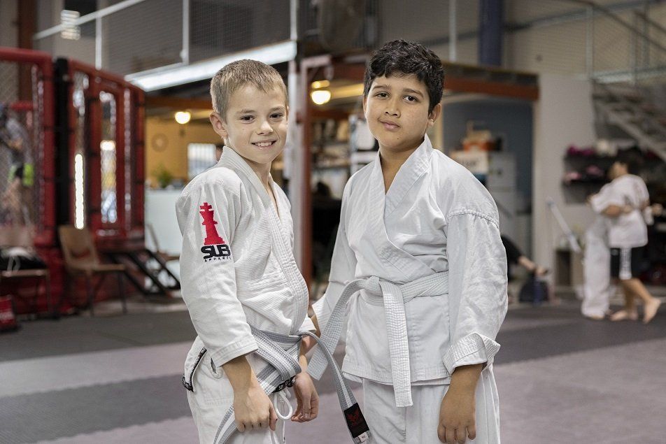 Two young boys in karate uniforms are standing next to each other in a gym.