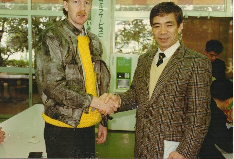 A man in a plaid jacket shakes hands with another man