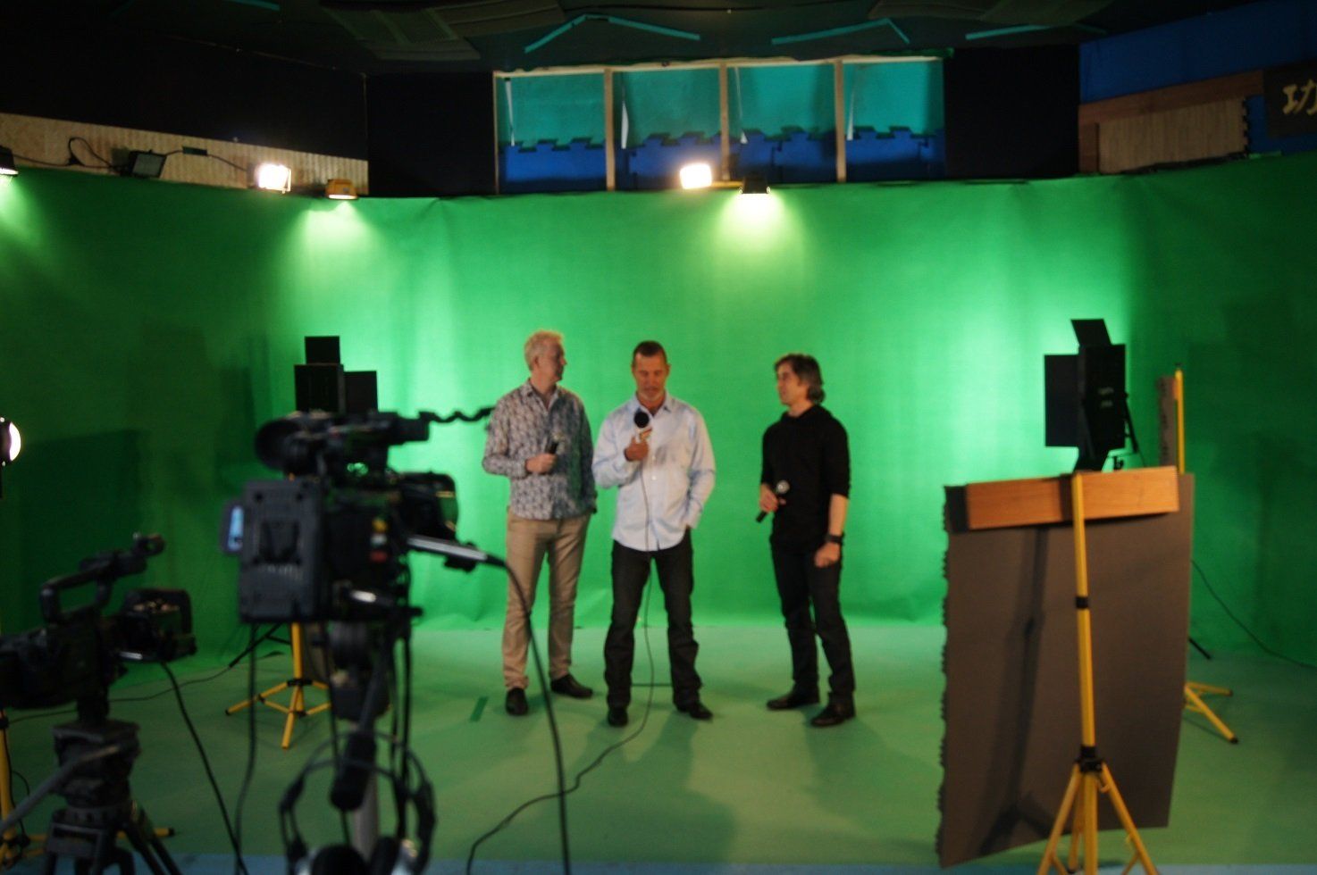 Three people are standing in front of a green screen