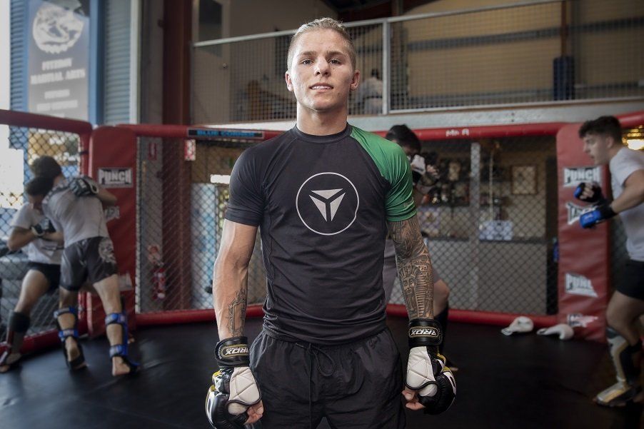 A man is standing in front of a boxing ring in a gym.