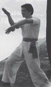 A man in a white shirt and white pants is practicing martial arts.