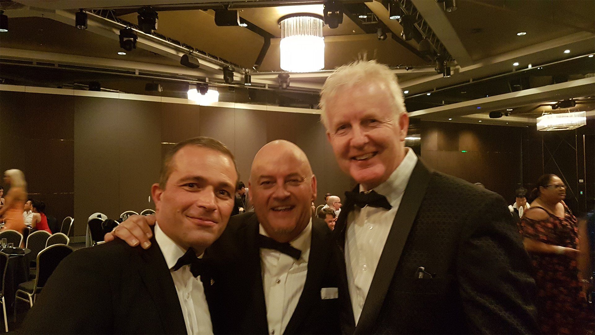 Three men in tuxedos are posing for a picture in a dark room.