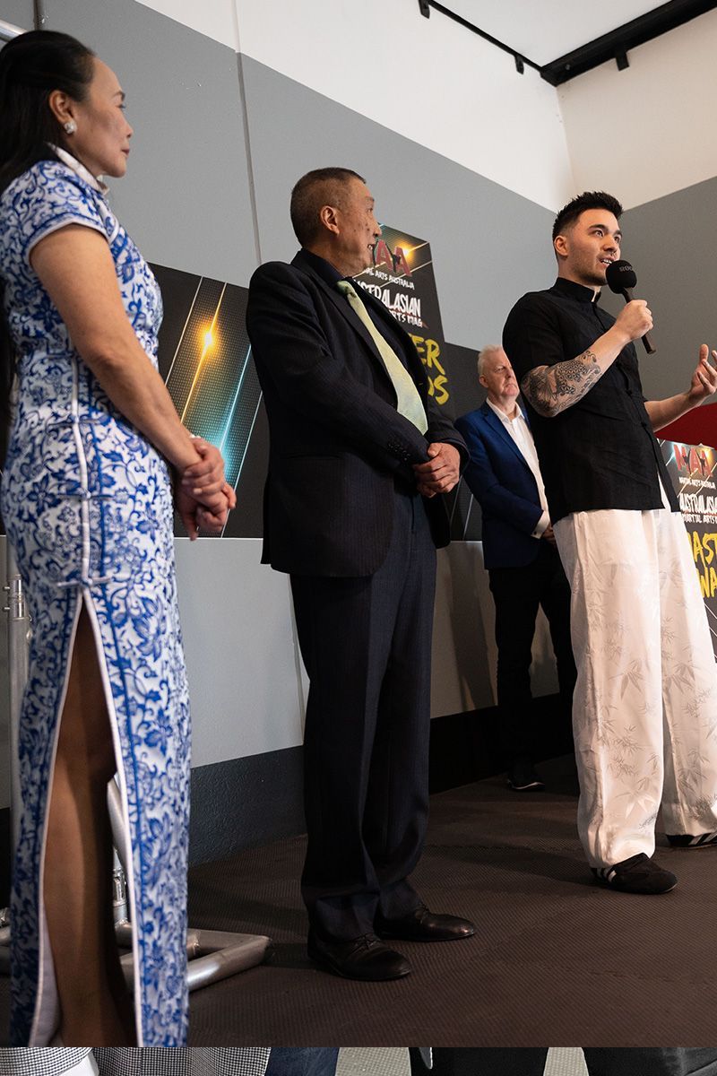 A man is speaking into a microphone while standing next to a woman in a blue dress.