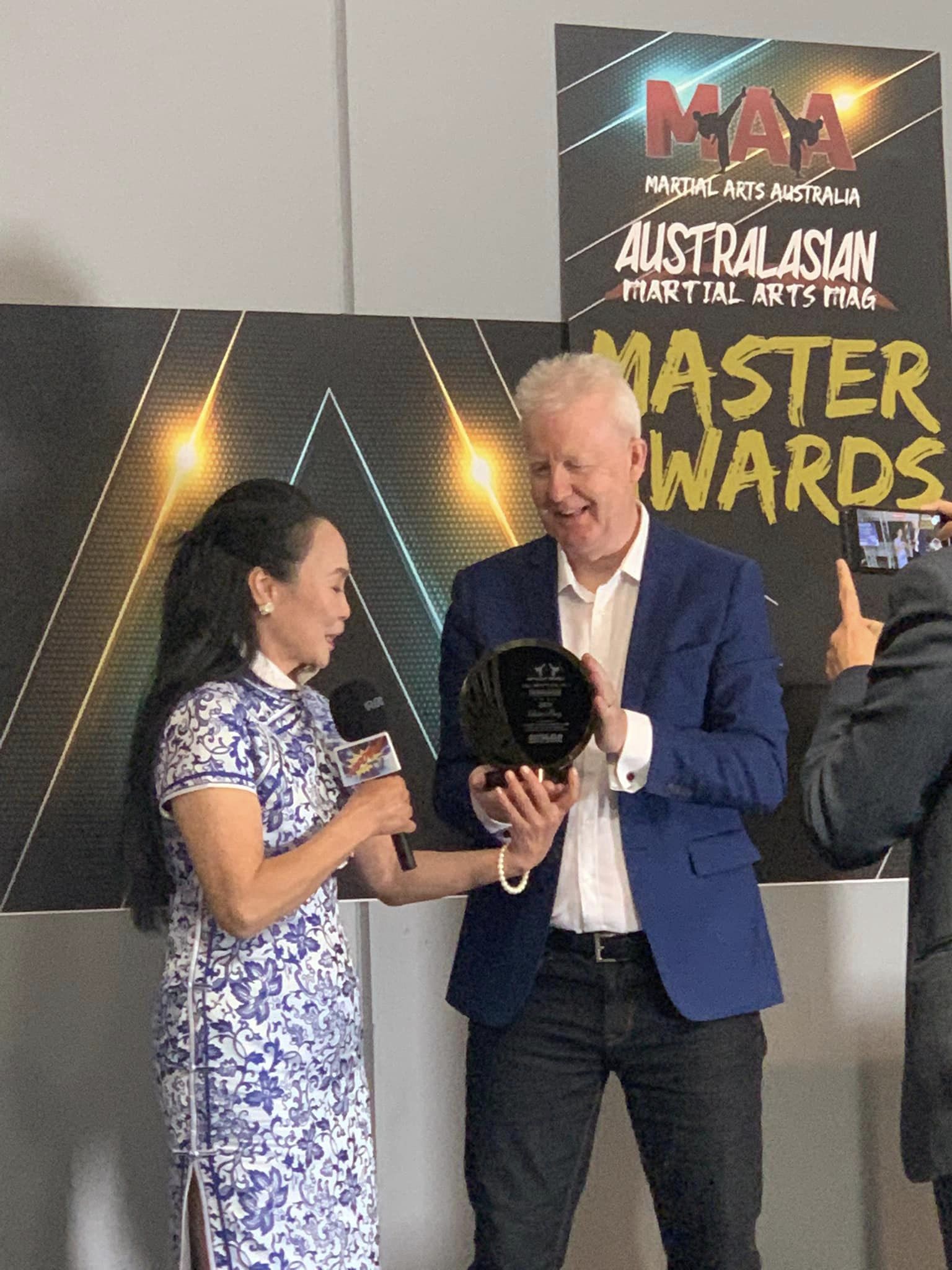 A man and a woman are standing next to each other holding a trophy.