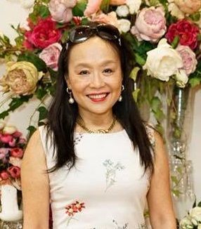 A woman in a white dress is smiling in front of a vase of flowers.