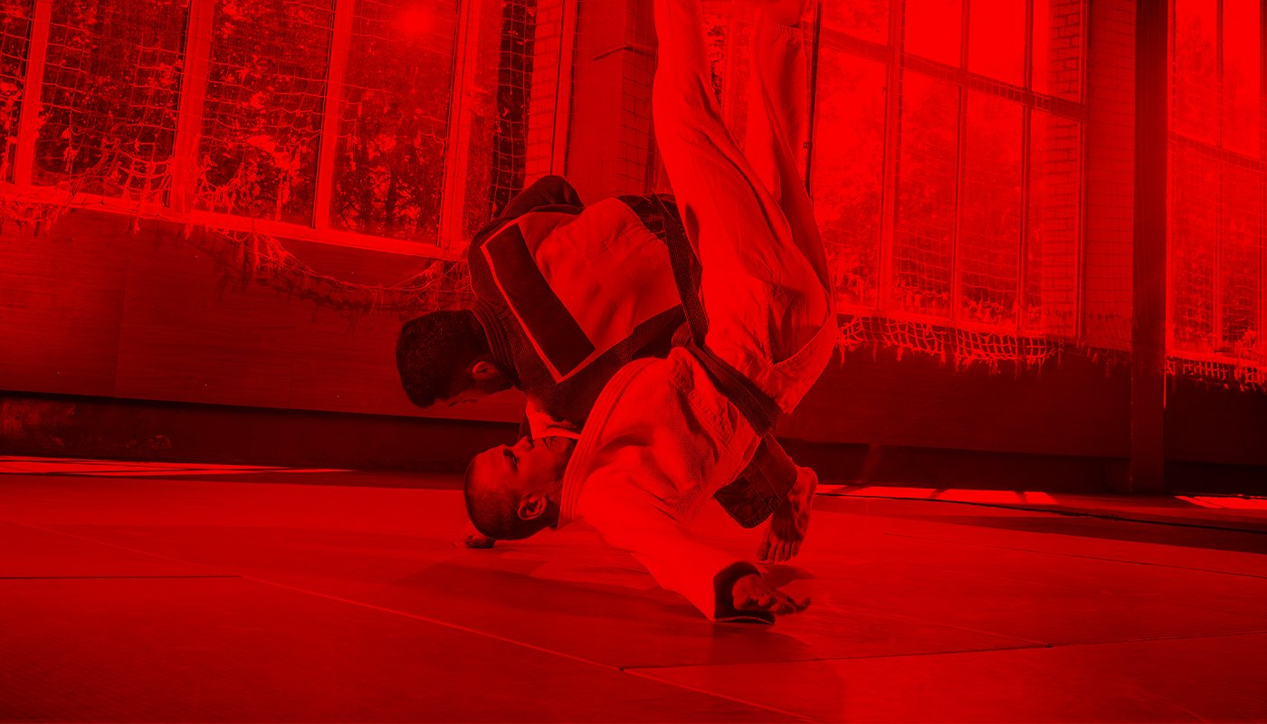 A man is doing a judo throw on a red background.