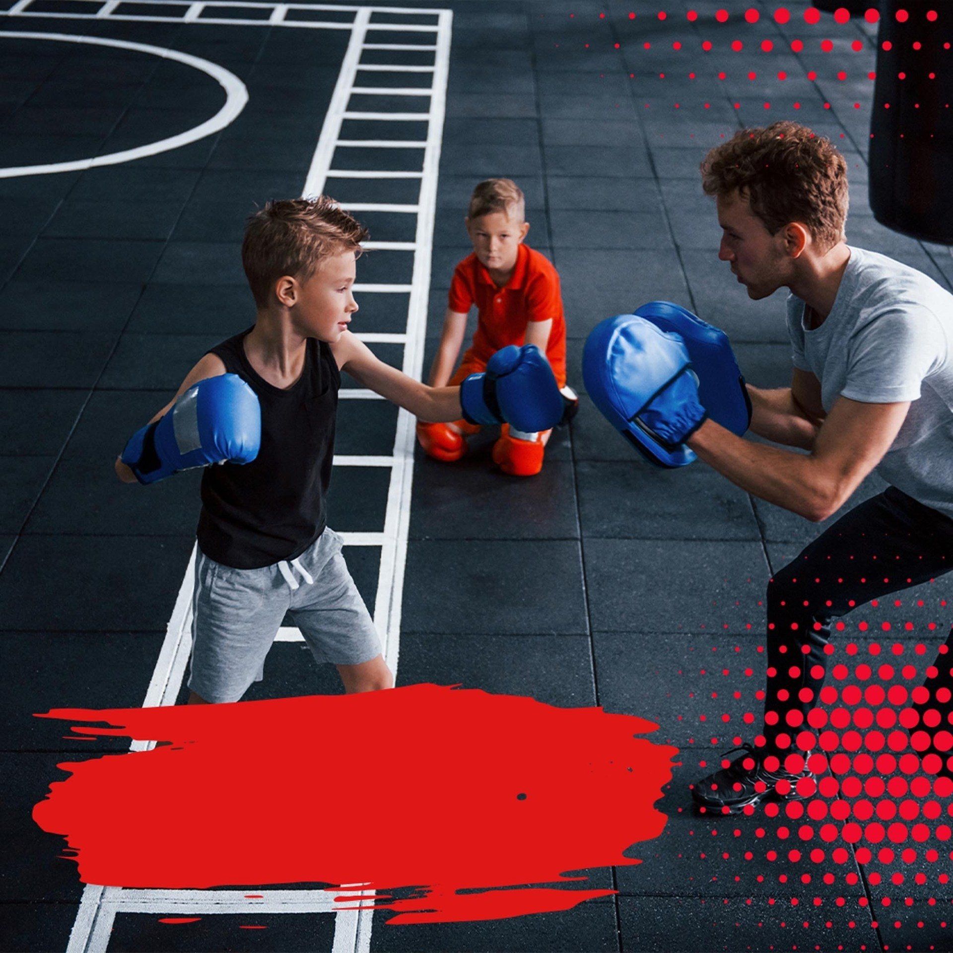 A man is teaching two young boys how to box in a gym.