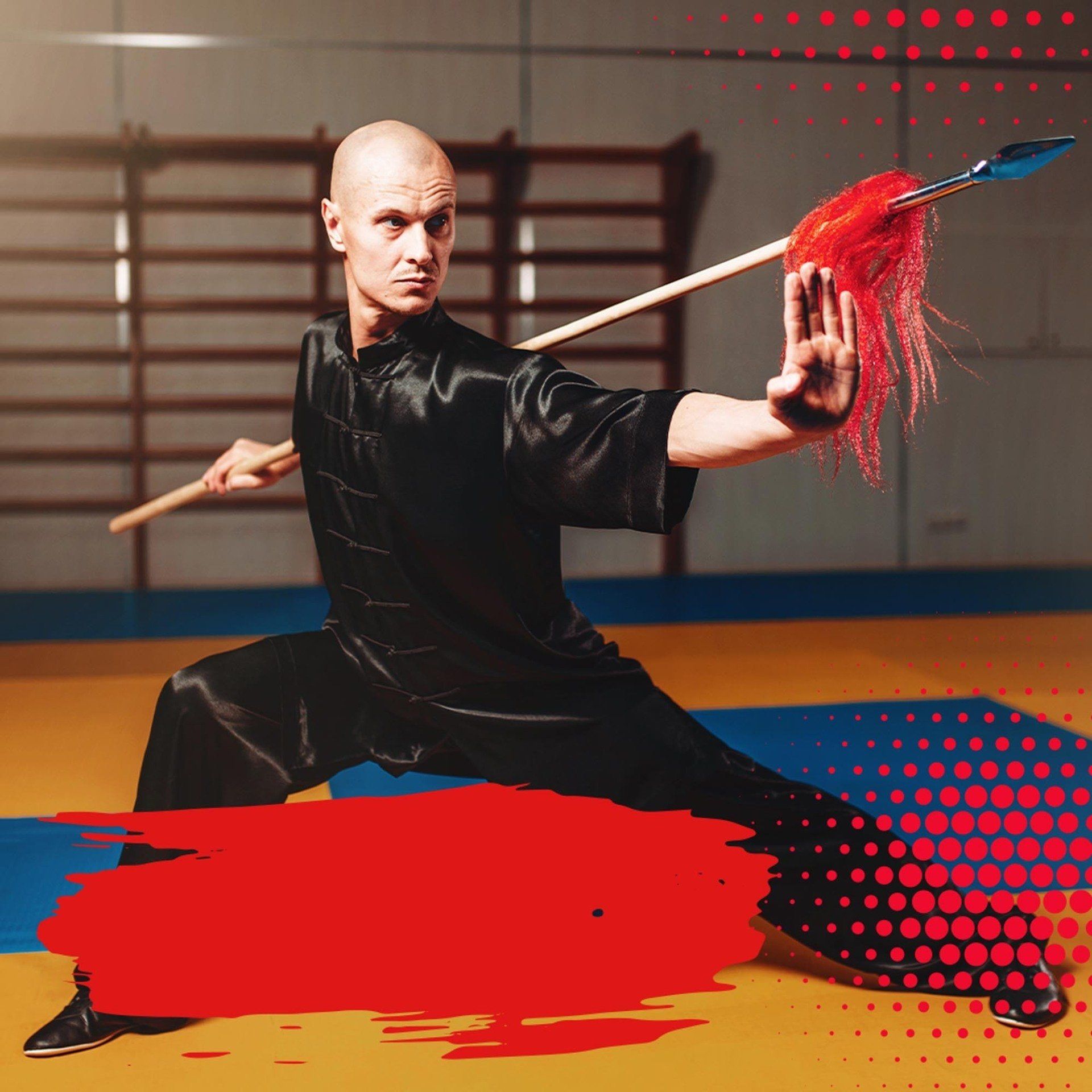 A man is practicing martial arts with a stick in a gym.