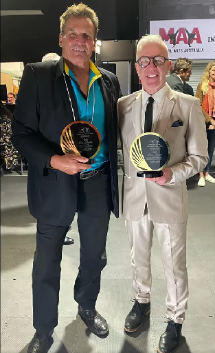 Two men in suits are standing next to each other holding trophies.