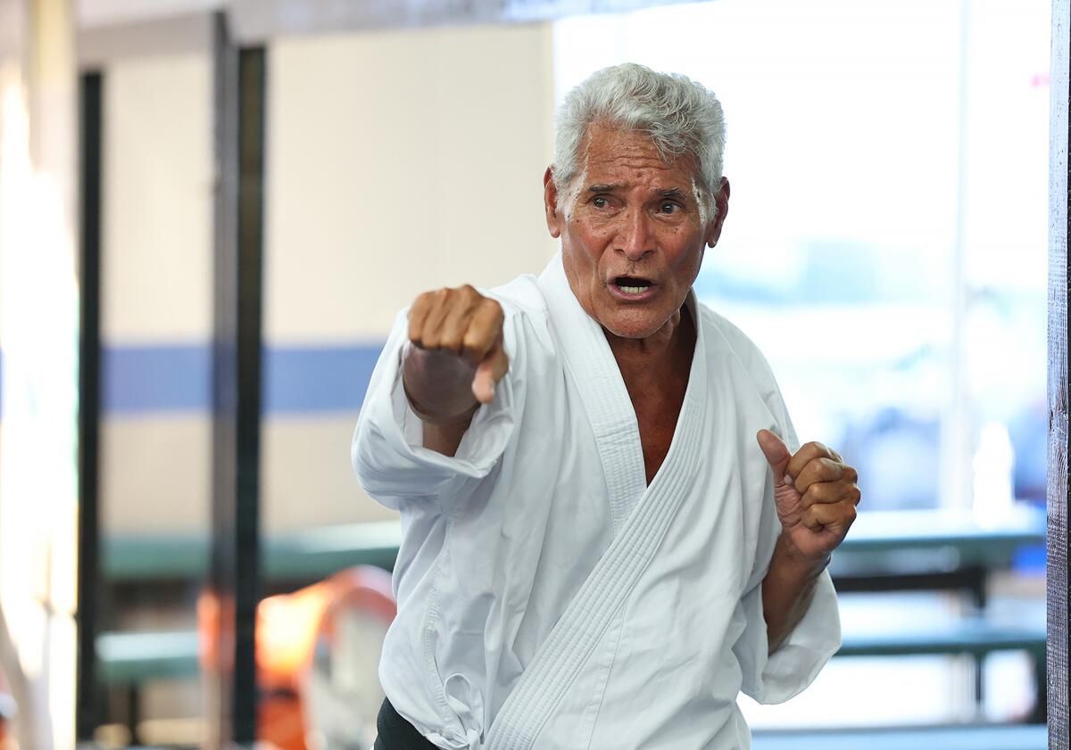 Elderly man in karate uniform, punching forward with focused expression in a dojo.