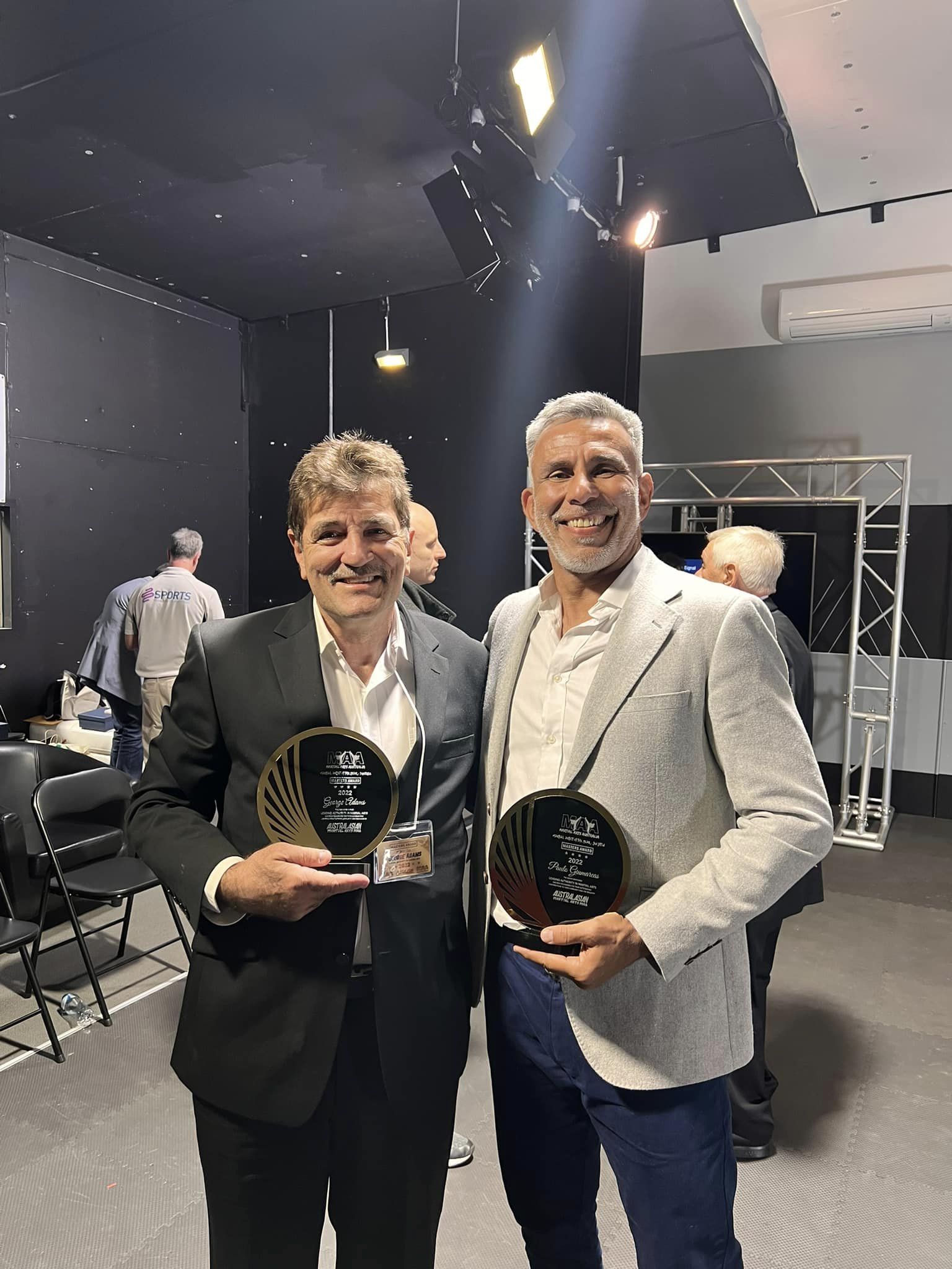 Two men are standing next to each other holding trophies.