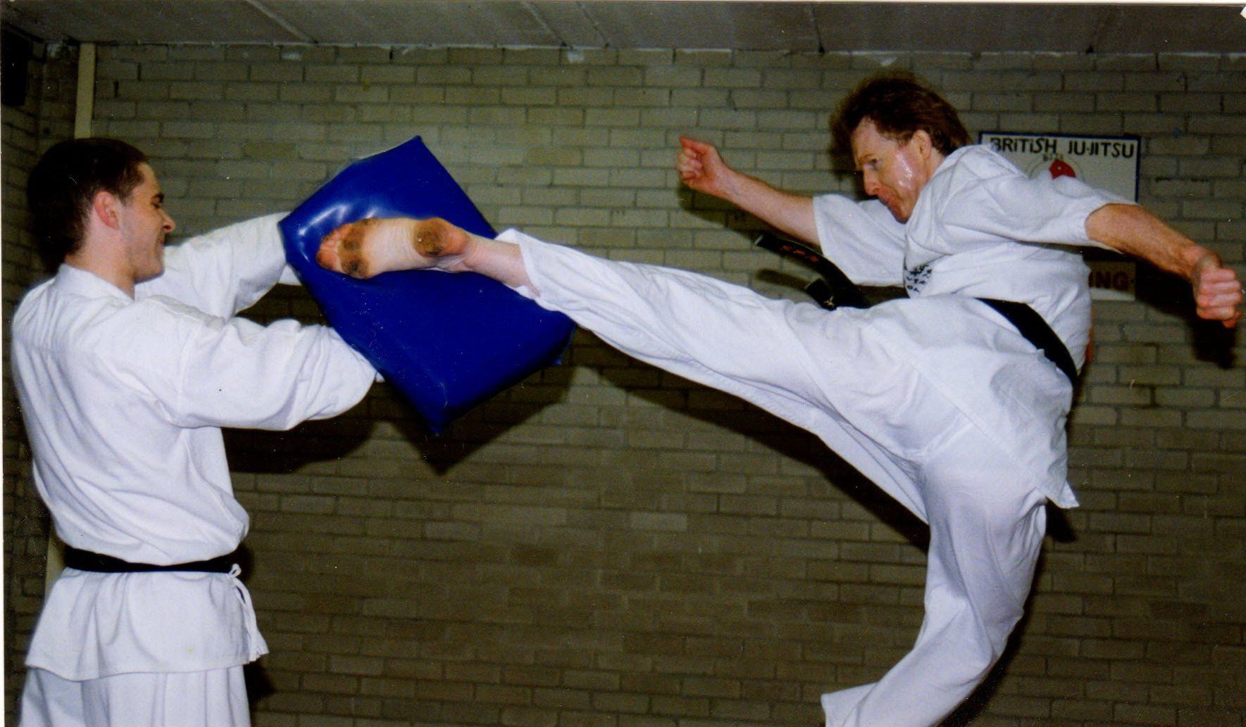 A man kicking a blue pillow while another man watches