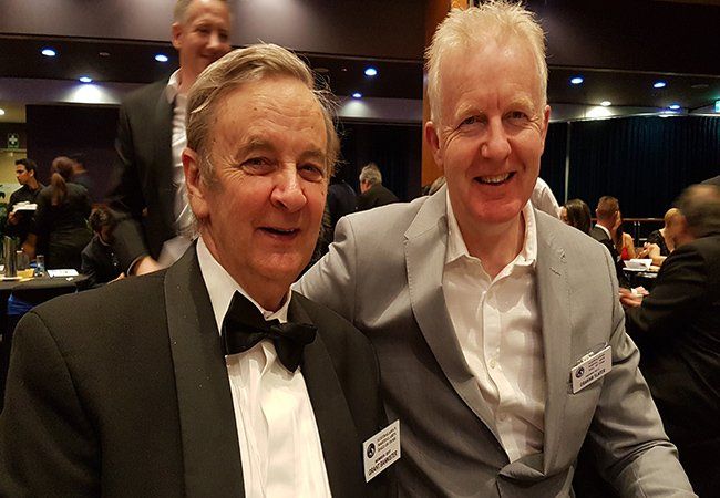 Two men in suits and bow ties are posing for a picture.