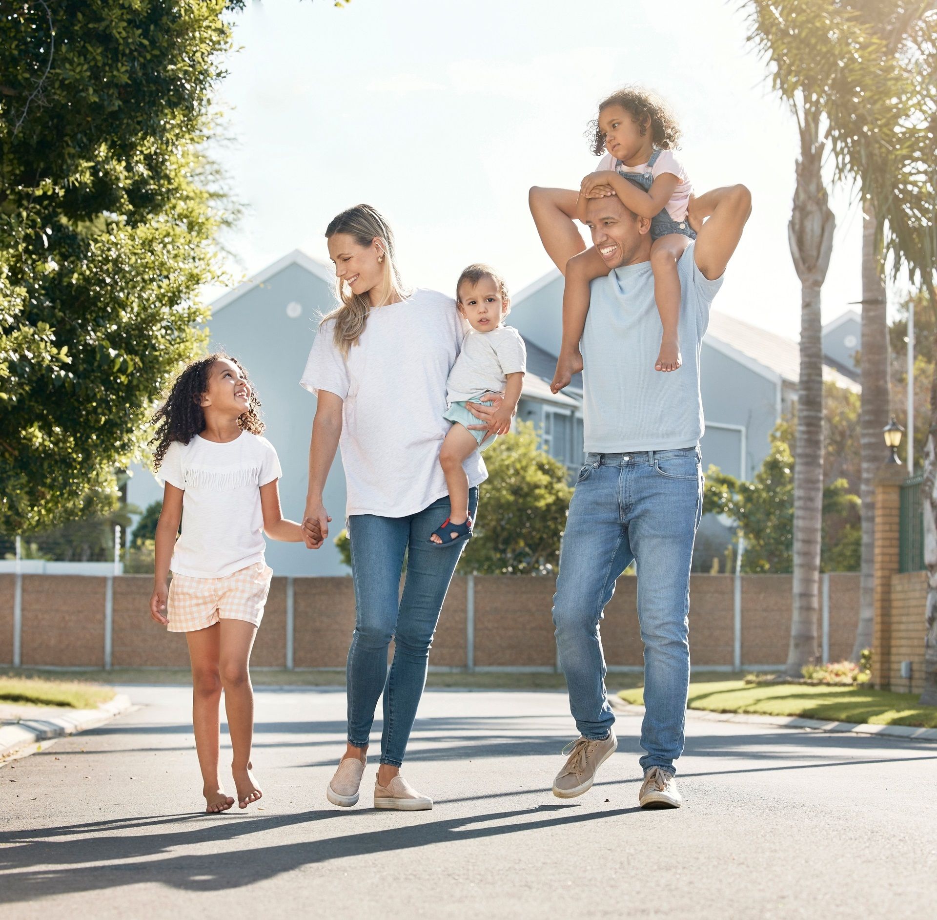 A family is walking down the street with a man carrying two children on his shoulders.