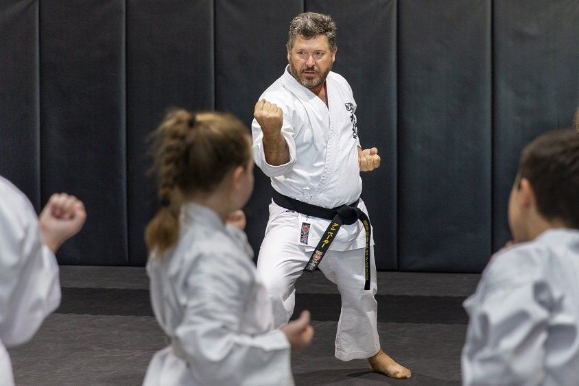 A man in a white karate uniform is teaching a group of children.
