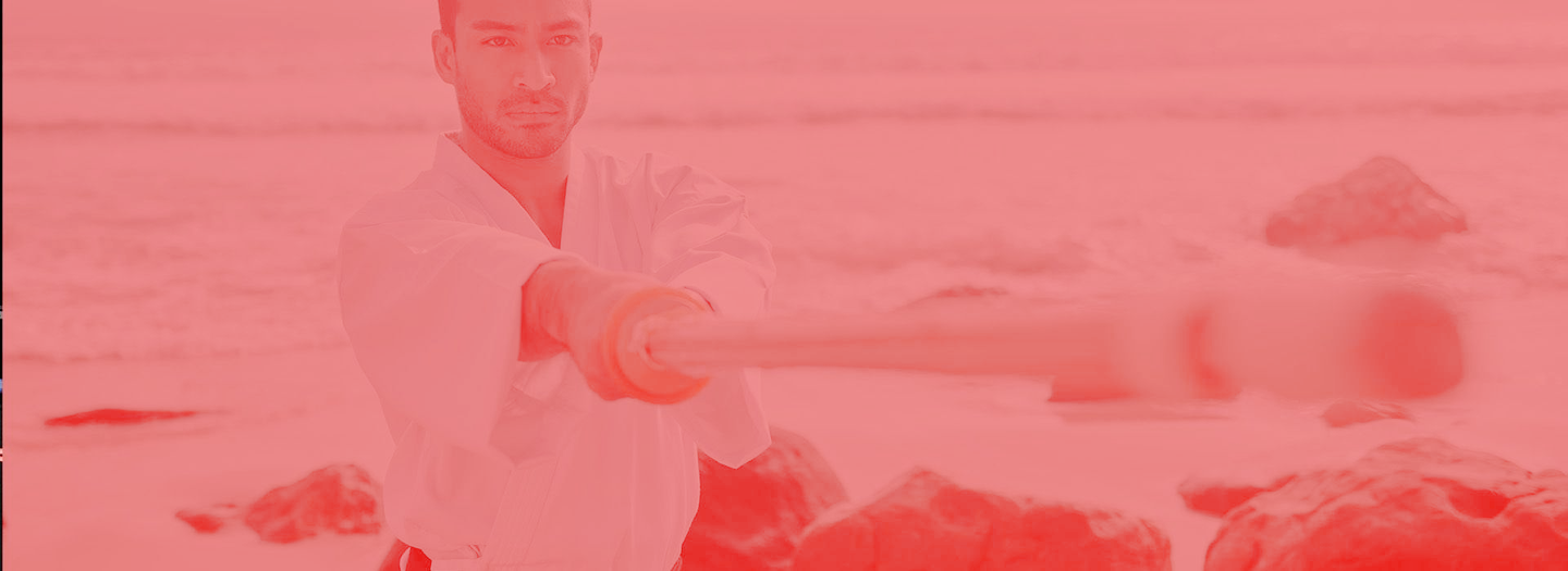 A man in a white karate uniform is standing on a beach.