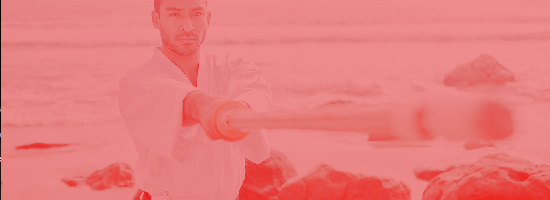A man in a white karate uniform is standing on a beach.