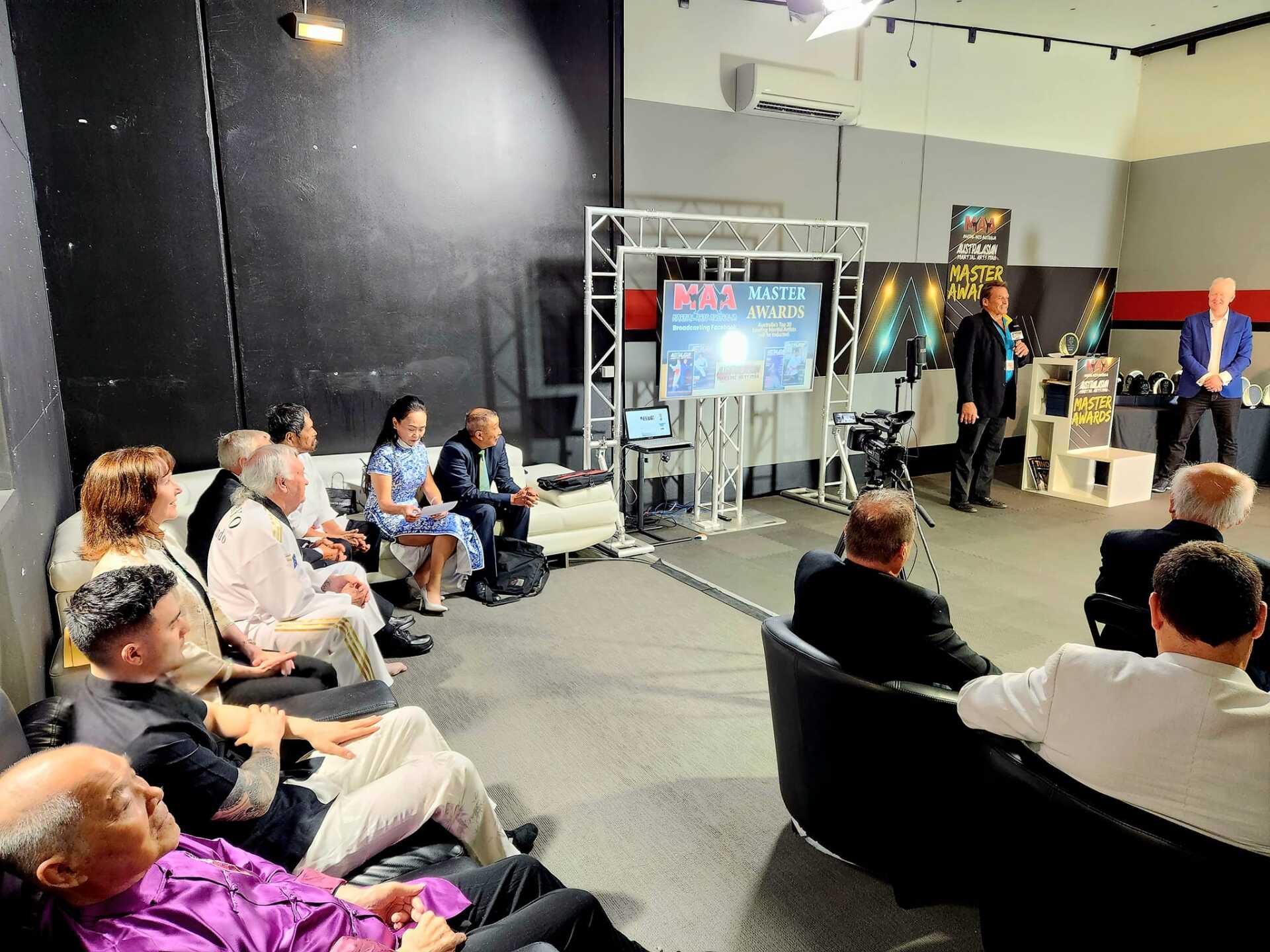 A group of people are sitting in chairs in a room with a man standing in front of them giving a presentation.