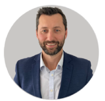 A man with a beard is wearing a blue suit and white shirt.