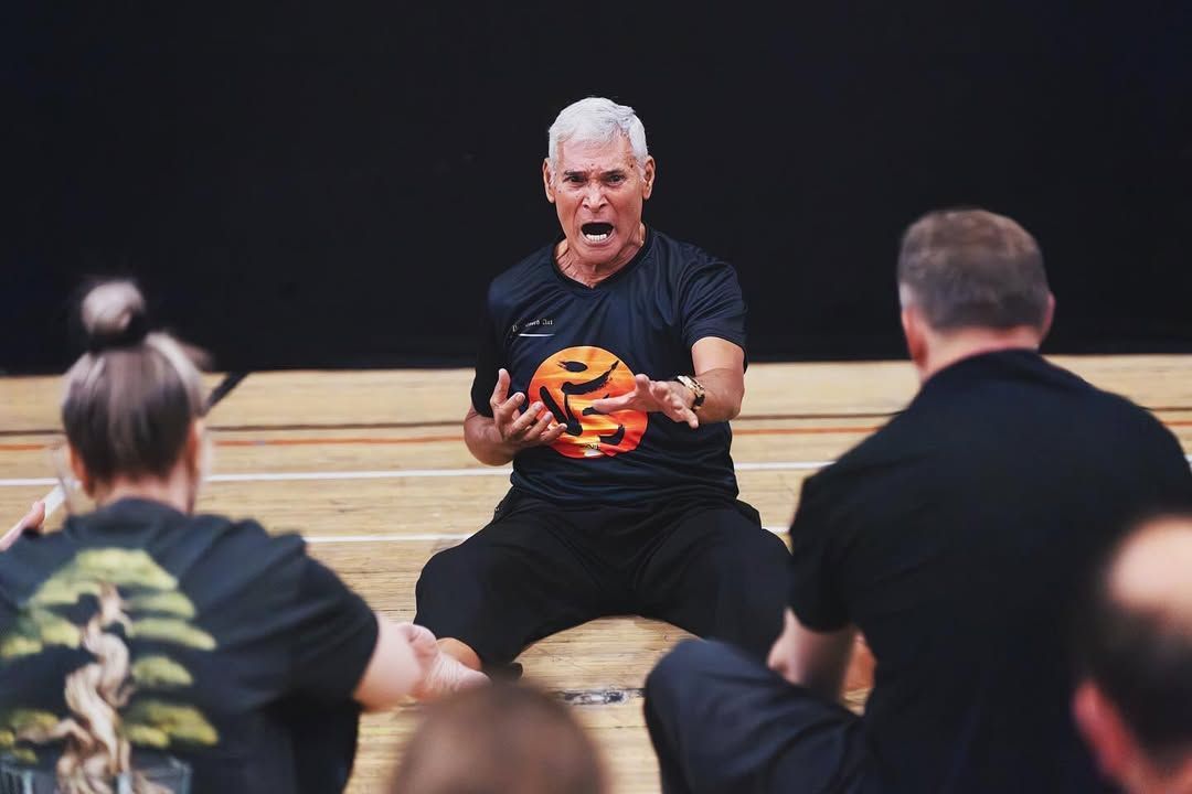 Man in black shirt, yelling with orange object, in front of people, possibly in a class or performance.