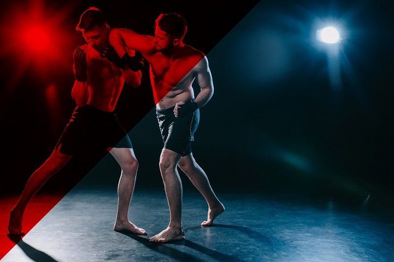 Two men are fighting in a ring in a dark room.