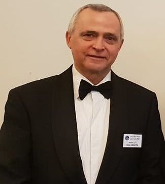 A man in a tuxedo and bow tie is standing in front of a white wall.