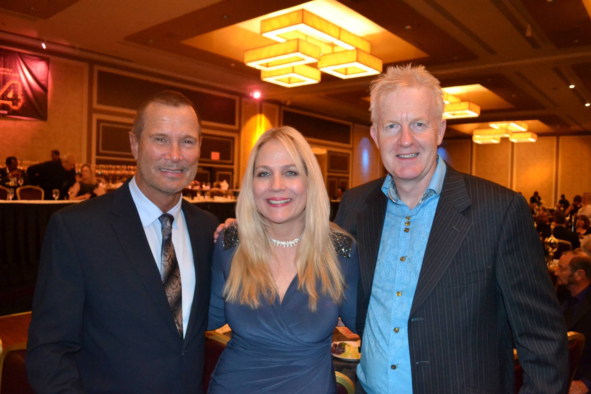 Two men and a woman are posing for a picture in a large room.