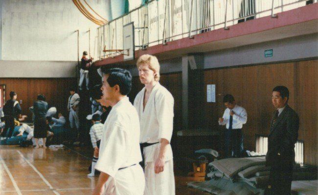 A group of people are standing in a gym with a basketball hoop in the background