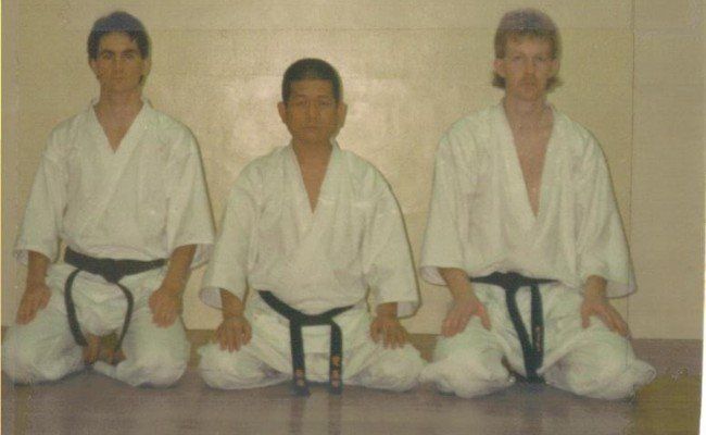 Three men wearing white karate uniforms and black belts pose for a picture