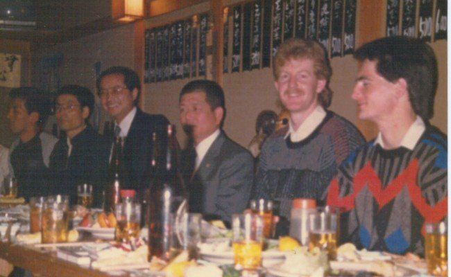 A group of men are sitting at a table with drinks and food