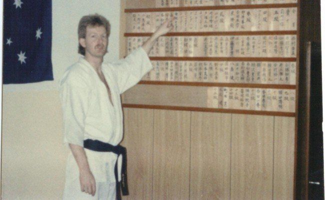 A man in a karate uniform points to a wall of cards
