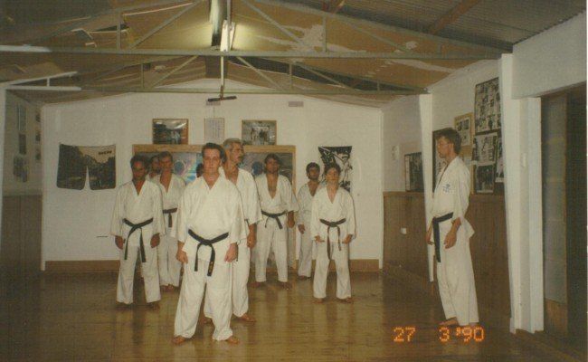 A group of men in white karate uniforms are standing in a room with the date 27 3 1990