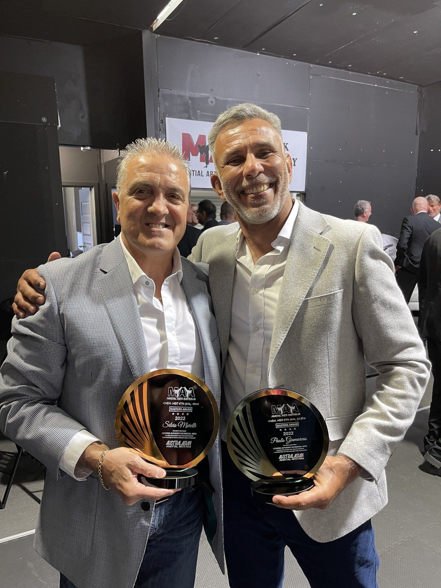 Two men are posing for a picture while holding trophies.