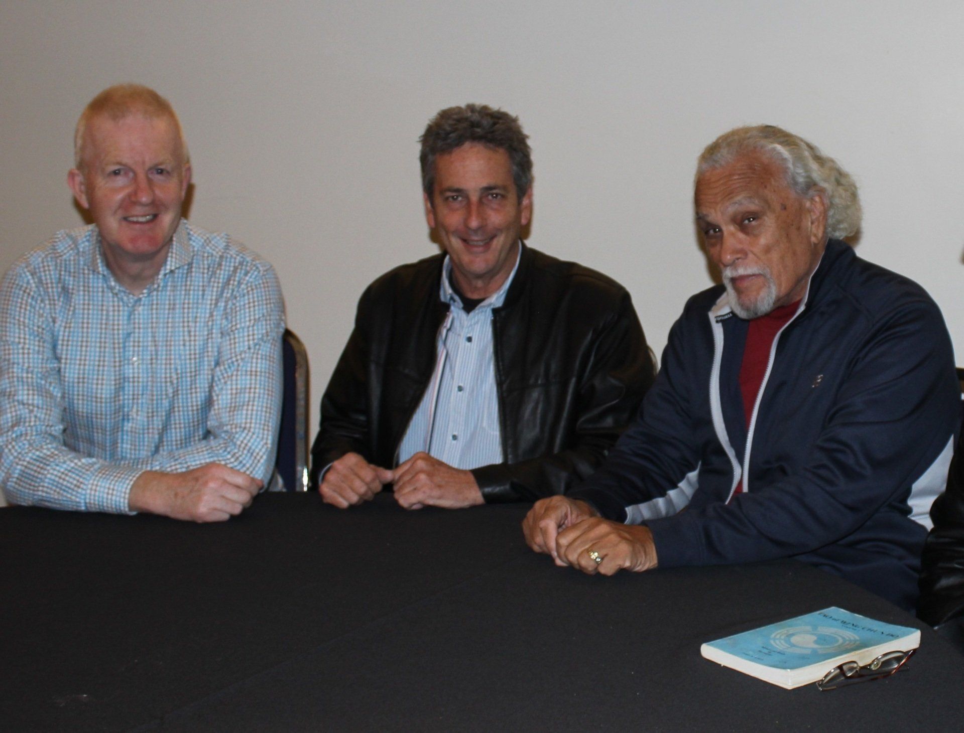 Three men are sitting at a table with a book on it