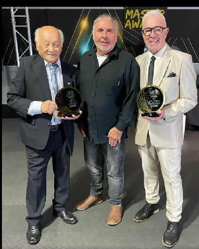 Three men are standing next to each other holding trophies.