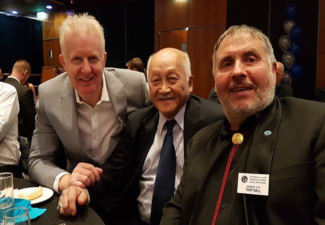 Three men are posing for a picture while sitting at a table.