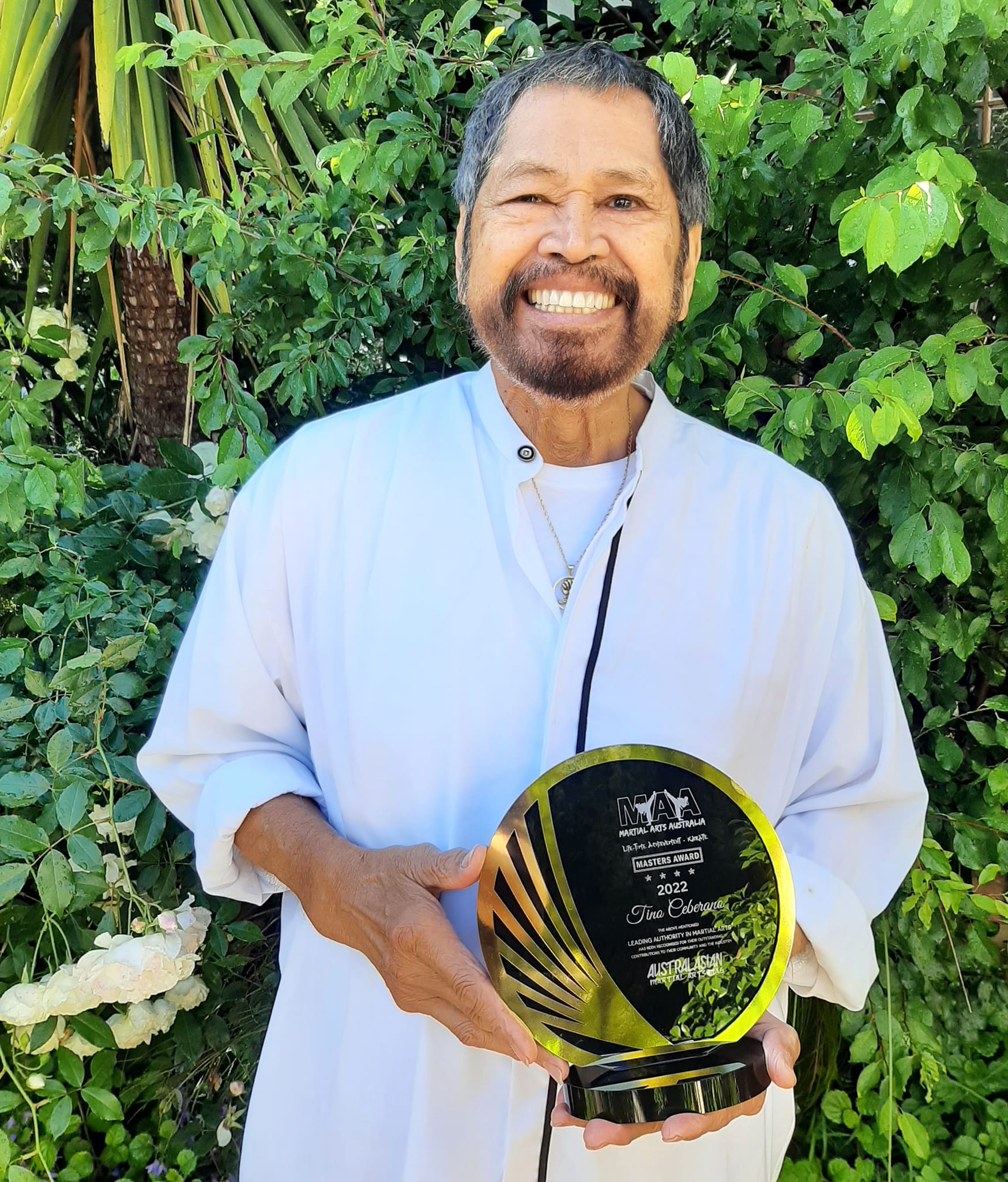 A man in a white robe is holding a trophy and smiling.